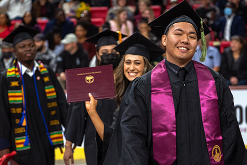 A graduate smiles as he receives his diploma