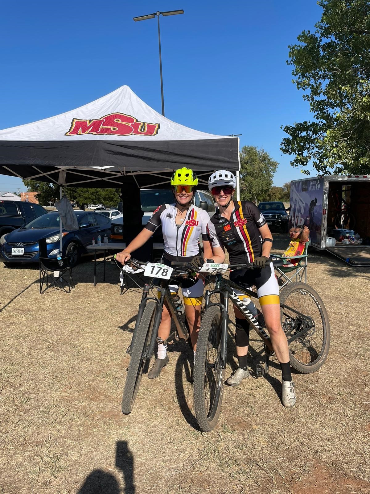 MSU Texas cyclists stand on their bikes in front of the MSU tent