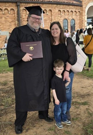 Jonathan Hull stands outside of D.L. Ligon Coliseum after his graduation, joined by his wife, Mindy, and son, Luke