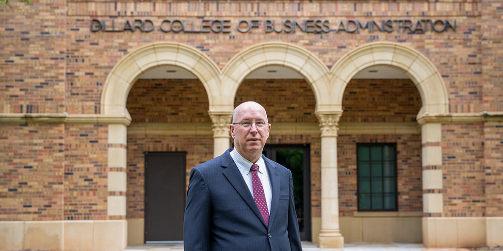 Jeff Stambaugh in front of Dillard College of Business Administration sign and brick building