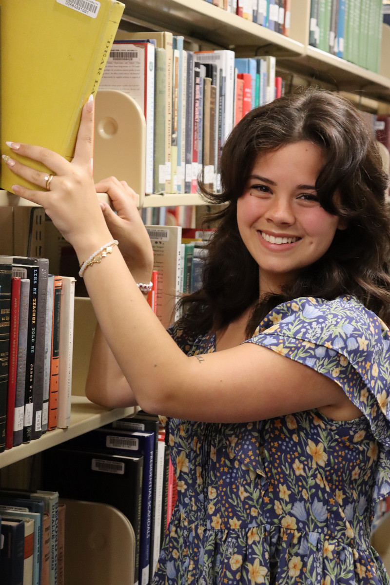 Carley Mitchell stands by a book case