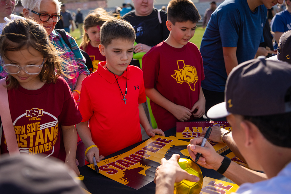 Players sitting at table give autographs to supporters