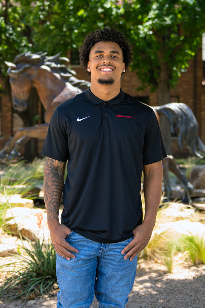 Devean Isaac standing with jeans and his graduation attire