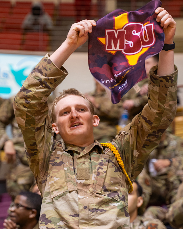 Military member holds up MSU flag in support of the Mustangs at Miliary Appreciation Game in 2025