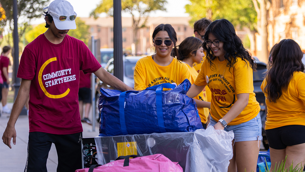 Move-In Day participants move materials, including one volunteer with a t-shirt reading 'Community Starts Here' in a maroon shirt